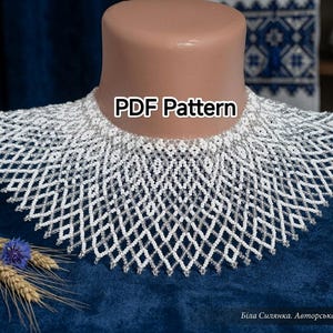 Può includere: Una collana a colletto di perline bianche con un complesso motivo a losanghe. Il testo 'PDF Pattern' è visibile al centro. Il pezzo è esposto su un manichino a forma di collo, mettendo in risalto l'intricato design di perline intrecciate.