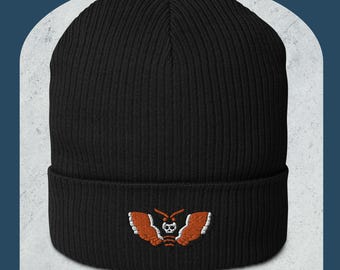 May include: Black knit beanie with a white and orange embroidered moth design. The moth has a skull and crossbones on its body.