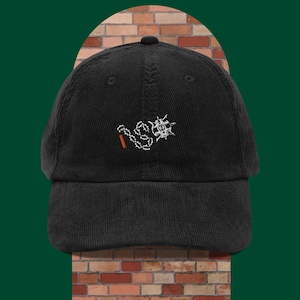 May include: Black corduroy baseball cap with an embroidered design of a chain and a bomb. The design is in white thread.