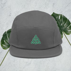 May include: A gray 5-panel cap with a green embroidered Celtic knot design.