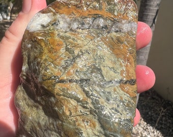 May include: A large, irregularly shaped rock with a smooth, polished surface. The rock is a mix of green, brown, and white colors with a swirling pattern.