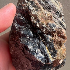 Puede incluir: Una roca grande, de color gris oscuro, rugosa y de forma irregular, con algunas vetas de color gris claro y marrón.