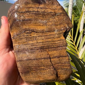 May include: A smooth, rounded, brown and tan striped rock with a natural, polished finish.