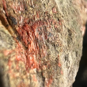 Op de afbeelding: Close-up van een rotsformatie met een roodbruine mineraalafzetting. De rots heeft een ruw, getextureerd oppervlak en een lichtgrijze kleur.