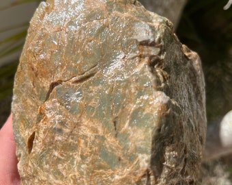 May include: A rough, green and brown rock with a smooth, polished surface. The rock has a natural, organic texture.