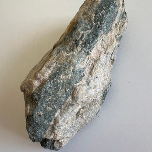 May include: A large, irregularly shaped rock with a mix of grey and green colours. The rock has a rough, textured surface.