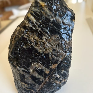 May include: A black and white striped rock with a smooth, polished surface. The rock has a natural, organic shape and is a unique piece of nature.