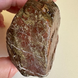 Puede incluir: Una roca de color marrón rojizo con vetas blancas y amarillas. La roca tiene una superficie rugosa y texturizada. La piedra natural se sostiene en una mano. Podría ser un objeto decorativo o de colección.