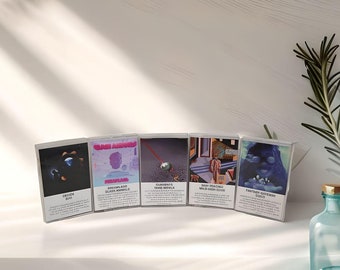 May include: Five cassette tapes with different album covers. The covers feature a variety of colors and designs, including a blue and black image of a planet, a pink and blue image of a person's face, a purple and blue image of a sphere, a blue and yellow image of a building, and a blue and purple image of a person's face. The tapes are all in clear plastic cases.