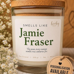 Puede incluir: Una vela en vaso de cristal transparente con tapa de corcho y una etiqueta blanca que dice "SMELLS LIKE Jamie Fraser" y "The man every woman would cross centuries for." La etiqueta incluye "Soy Coconut | 250 gr | 9oz | 40 h+". Una etiqueta redonda marrón dice "PERSONALISATION AVAILABLE".