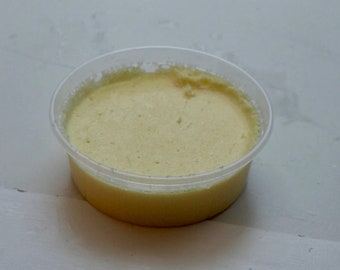 Può includere: Un piccolo contenitore di plastica trasparente riempito con una sostanza cremosa di colore giallo pallido.