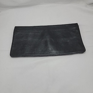 May include: A black leather clutch with a rectangular shape. The clutch has a smooth, slightly textured surface and a simple, minimalist design. The clutch is closed and appears to be empty.