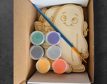 May include: A craft kit in a cardboard box, containing wooden cutouts of a ghost and other shapes, six paint pots in various colours, and a paintbrush. The wooden cutouts are unpainted. The paint colours include green, purple, grey, white, yellow, and orange.