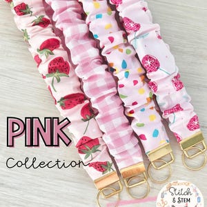 Könnte beinhalten: Rosa Stoff-Schlüsselanhänger mit goldfarbener Hardware. Die Schlüsselanhänger weisen verschiedene rosa Muster auf, darunter Erdbeeren, Vichy-Karo und Konfetti. Der Text "PINK Collection" wird im Bild angezeigt.