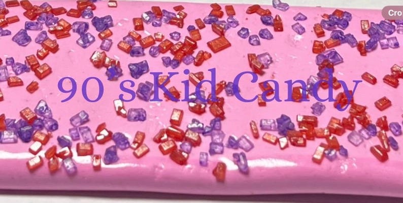 May include: Pink candy bar with red and purple sprinkles. The text "90's Kid Candy" is printed on the candy bar.