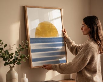 Puede incluir: Una impresión artística enmarcada con un sol amarillo y rayas azules horizontales. La obra de arte está en un marco de madera clara y se muestra contra una pared beige. Estilo minimalista.