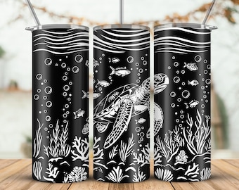Könnte beinhalten: Ein schwarzer Becher mit einem weißen Meeresschildkröten-Design, Fischen, Blasen und Wasserpflanzen. Der Becher hat einen silbernen Deckel und einen Strohhalm. Das Design umschließt den gesamten Becher.