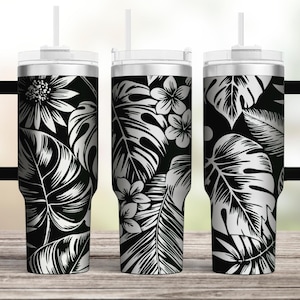 Puede incluir: Tres vasos de acero inoxidable con diseños de hojas y flores tropicales en blanco y negro. Los vasos tienen tapas y pajitas. El vaso de la izquierda tiene un asa negra.