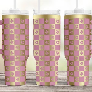 May include: Three stainless steel tumblers with a pink and gold checkered pattern and a gold rim. The tumblers have a handle and a straw.