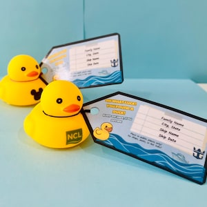 May include: Two yellow rubber duck toys with orange beaks and black eyes are next to two luggage tags. One duck has a Mickey Mouse logo, the other has an NCL logo. The tags have text that reads "OH WHAT LUCK! YOU FOUND A DUCK!" and space for personal information.