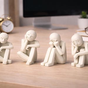 May include: Four off-white figurines depicting different emotional states: anger, happiness, sadness, and despair. The figures are seated with their heads resting on their hands. The figurines are on a light-colored wooden surface.