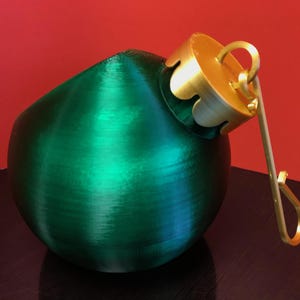 May include: A green Christmas ornament with a gold top and a gold hook. The ornament is made of a smooth, shiny material.