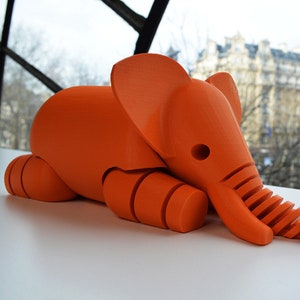 May include: A bright orange 3D printed elephant figurine with a segmented trunk. The elephant is lying down with its head resting on its front legs.
