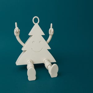 May include: A whimsical, off-white Christmas tree figurine with arms, legs, and a smiling face. The tree is gesturing with both hands, displaying the middle finger. The figurine has a loop at the top for hanging and is set against a teal background.