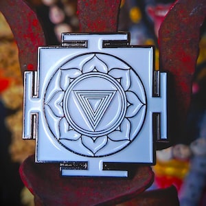 May include: A white and silver square pendant with a central circular design featuring a triangle within a lotus flower pattern. The pendant has a silver border and is set against a rusty, textured background.