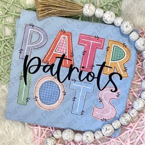 Puede incluir: Camiseta azul claro con la palabra "Patriots" en letras coloridas estilo patchwork. Las letras están delineadas en blanco y cosidas con hilo negro. La camiseta está decorada con una guirnalda de cuentas y una borla.