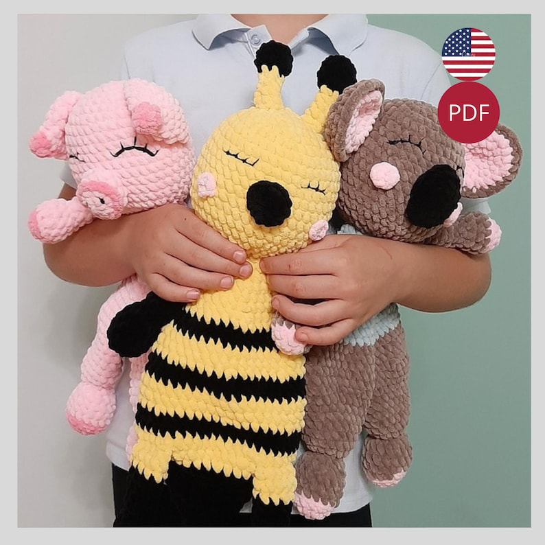 May include: Three handmade crochet stuffed animals: a pink pig, a yellow bee with black stripes, and a brown koala. Each plush toy has closed eyes, suggesting sleep. The toys are held in front of a person.