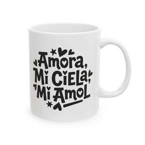 May include: White ceramic mug with black text reading "Amora, Mi Ciela, Mi Amol", decorated with hearts and stars. The mug features a curved handle and a glossy finish.