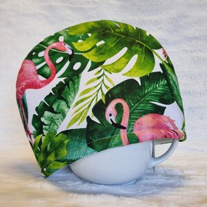 Puede incluir: Una tapa de tazón blanca con un estampado tropical con flamencos rosas y hojas de palmera verdes.