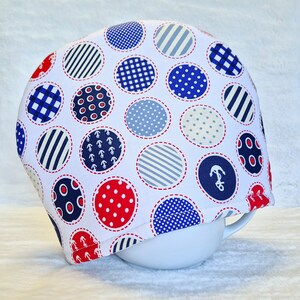 May include: White fabric bowl cover with a nautical theme. The cover is decorated with red, blue and white polka dots, stripes and anchors.