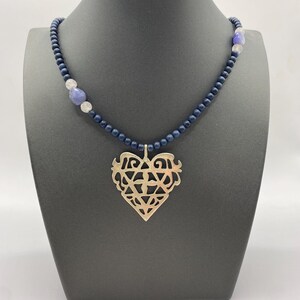 May include: A necklace with a silver heart pendant and blue and white beads. The heart pendant has a detailed, intricate design.
