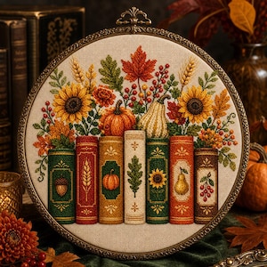 May include: A circular embroidery hoop containing a cross-stitch design of seven colourful book spines arranged in a row, topped with a vibrant autumn arrangement of sunflowers, pumpkins, maple leaves, wheat stalks, and red berries on a beige fabric.