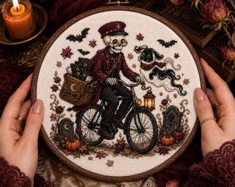 Op de afbeelding: Een ronde borduurring met een kruissteekontwerp van een skelet in een bordeauxrood uniform en pet op een fiets. Het skelet draagt een tas vol brieven, vergezeld door een spookhond, pompoenen en grafstenen.