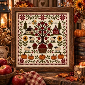 May include: A framed cross-stitch embroidery featuring a central apple tree, a house, a barn, four sheep, and pumpkins. The design includes baskets of apples, sunflowers, and a decorative border in red, green, and yellow on a cream fabric background.
