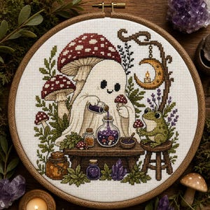May include: A cross-stitch embroidery in a wooden hoop featuring a white ghost pouring purple liquid from a small bottle into a glass jar on a table. A green frog sits on a stool nearby. The scene includes red mushrooms, a crescent moon, and crystals.