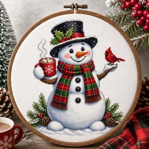 May include: A cross-stitch embroidery in a round wooden hoop featuring a snowman wearing a black top hat with holly, a red and green plaid scarf, and three black buttons. The snowman holds a red mug with a snowflake and a red cardinal bird.