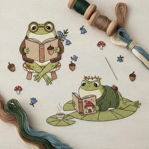 May include: Cross-stitch design featuring two whimsical frogs reading books. One frog wears glasses and sits on a mushroom, while the other relaxes on a lily pad. The design includes acorns, flowers, and embroidery thread.