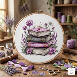 May include: A wooden embroidery hoop with a floral and book design. The design features a stack of books, purple flowers, and greenery. Embroidery floss, scissors, and other craft supplies are on a wooden table.