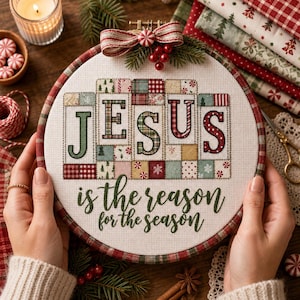 May include: A circular embroidery hoop containing a cross-stitch project on white fabric. The design features the word JESUS in large, patchwork-style letters, with the text is the reason for the season below. A red and white bow sits on top.