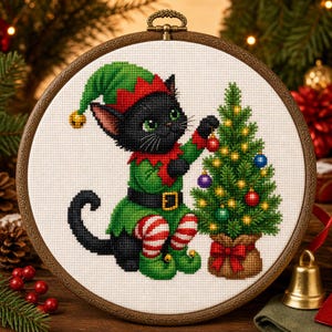 Può includere: Un telaio da ricamo circolare in legno contenente un disegno a punto croce di un gatto nero che indossa un costume da elfo verde e rosso con un cappello abbinato. Il gatto decora un piccolo albero di Natale con ornamenti colorati.