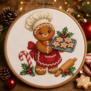 May include: A cross-stitch embroidery in a round wooden hoop featuring a gingerbread person wearing a white chef hat and a red apron. The figure holds a tray of star-shaped cookies, with a candy cane and a wooden rolling pin nearby.