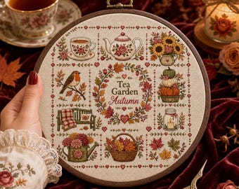 May include: A circular embroidery hoop containing a cross-stitch sampler on beige fabric. The design features the text Tea Garden Autumn surrounded by motifs including a teapot, teacup, robin, pumpkins, sunflowers, a bench, and a basket of leaves.