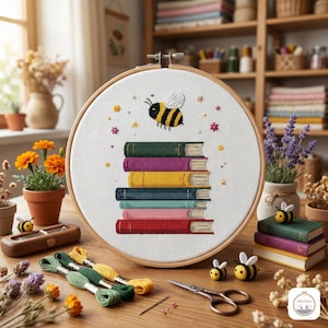 May include: A cross-stitch embroidery hoop featuring a stack of colorful books and a bee. The design includes a yellow, black, and white bee above the books. Embroidery floss, scissors, and bee-themed decorations are also present.