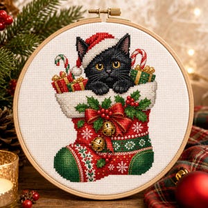 Può includere: Un ricamo a punto croce in un telaio di legno rotondo raffigurante un gattino nero con un cappello da Babbo Natale rosso e bianco, che spunta da una calza natalizia rossa e verde decorata con agrifoglio, un fiocco rosso e due campanellini dorati.