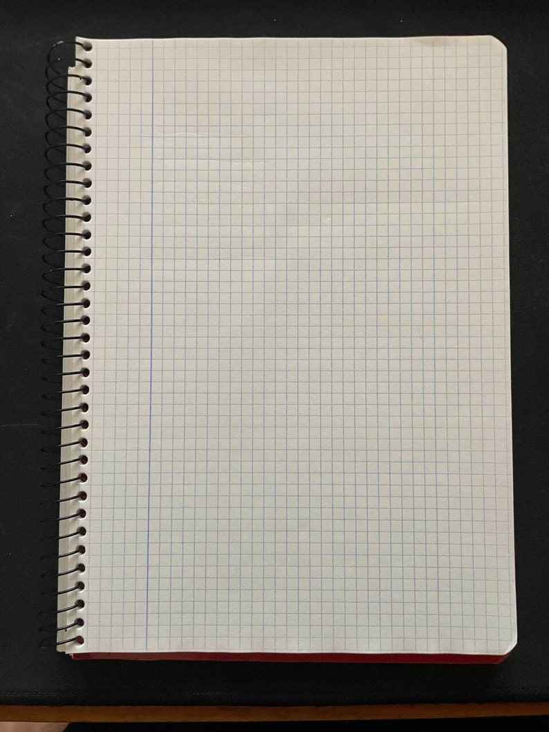 May include: A white spiral bound notebook with a grid pattern. The notebook has a red spine and a black plastic spiral binding.