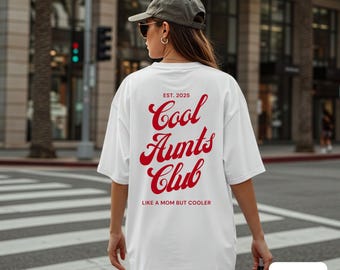 May include: White t-shirt with the text "Cool Aunts Club" in red script. The shirt also has the text "EST. 2025" above the main text and "LIKE A MOM BUT COOLER" below. The shirt is a casual, oversized style.